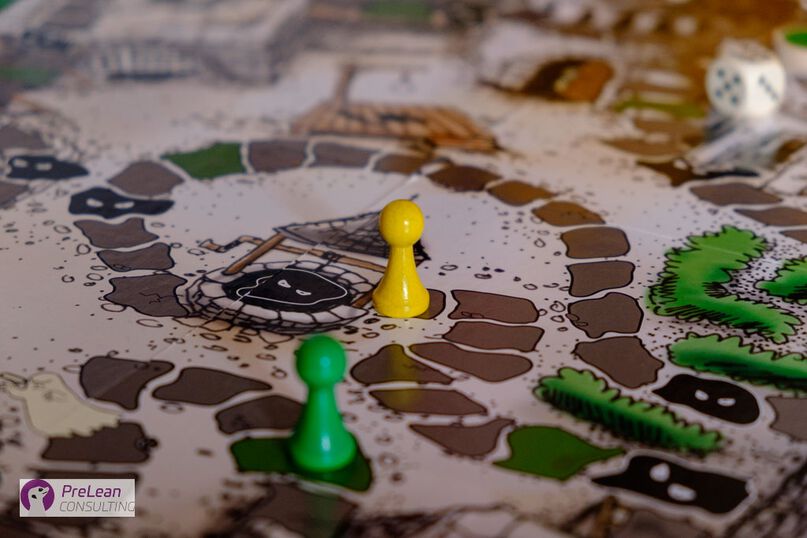Detailfoto vom Spielplan des Gesellschaftsspiels "Das schwarze Loch" mit einer gelben und einer grünen Spielfigur und Glückswürfel im Hintergrund